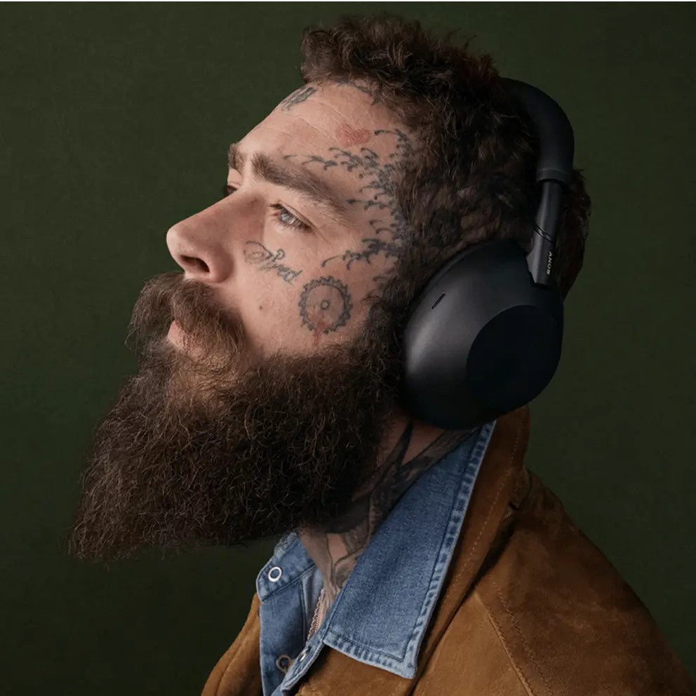 Man with tattoos and a beard wearing black headphones against a dark green background