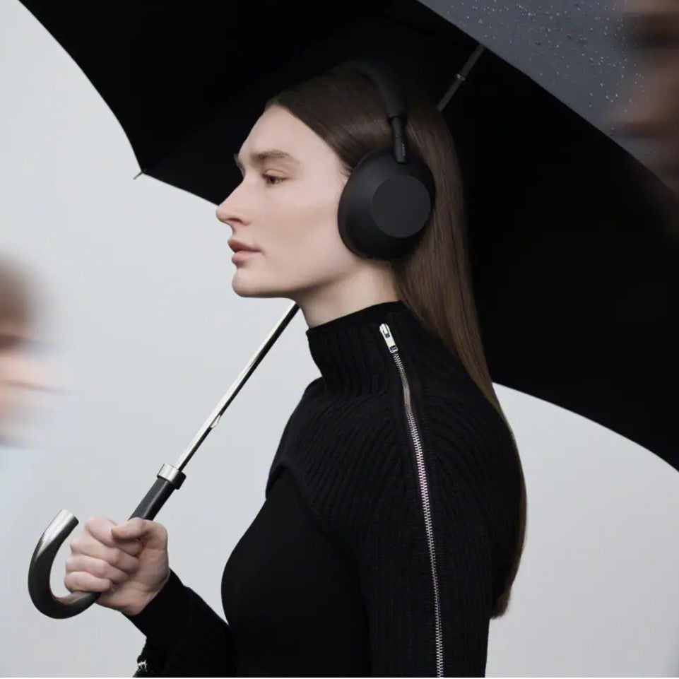 Woman wearing black headphones holding a black umbrella against a white background